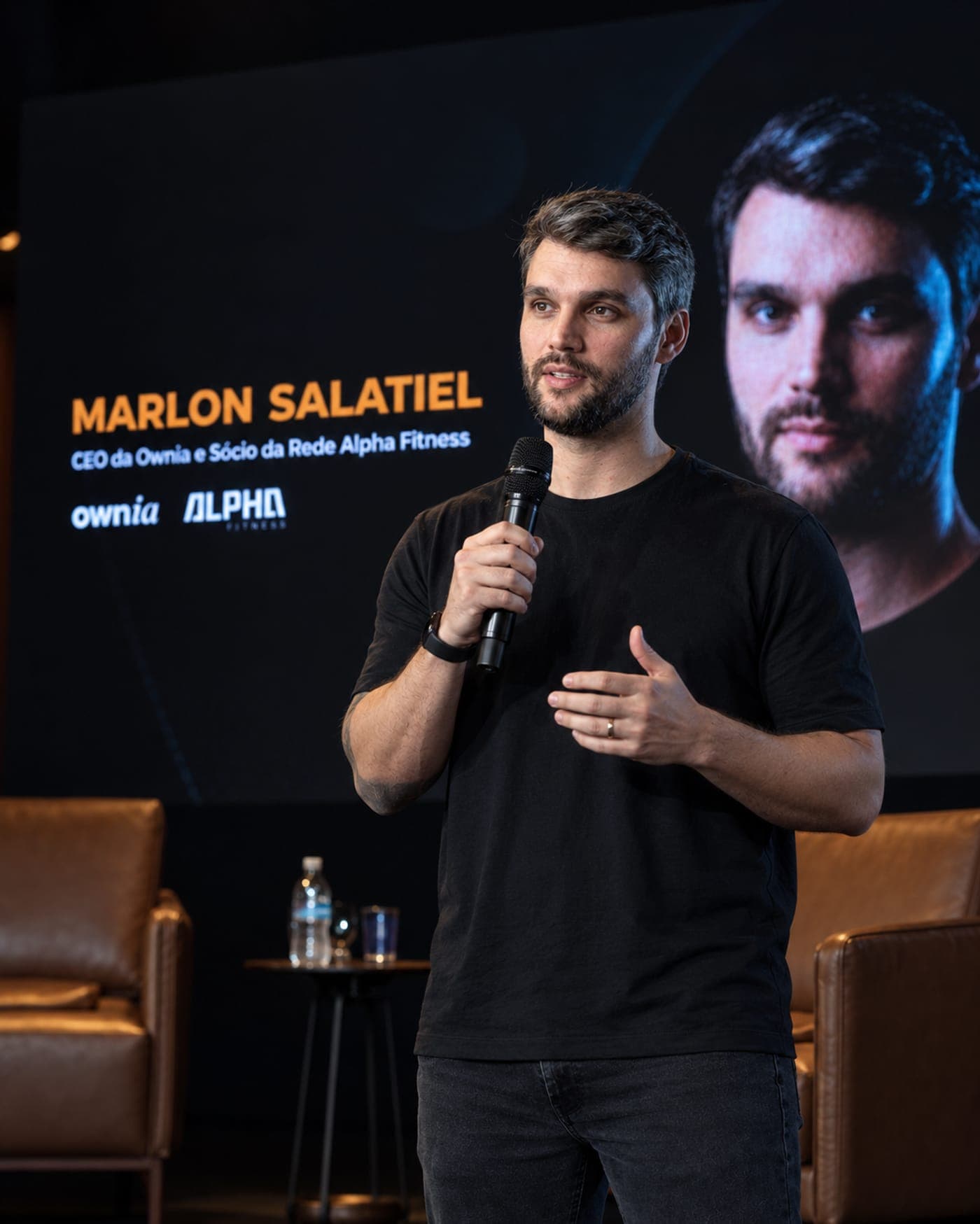 Marlon Salatiel falando ao microfone em um palco, com o nome e o cargo projetados ao fundo